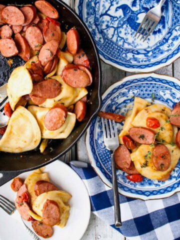 skillet of sausage and pierogis with blue plates on side. One plate is empty