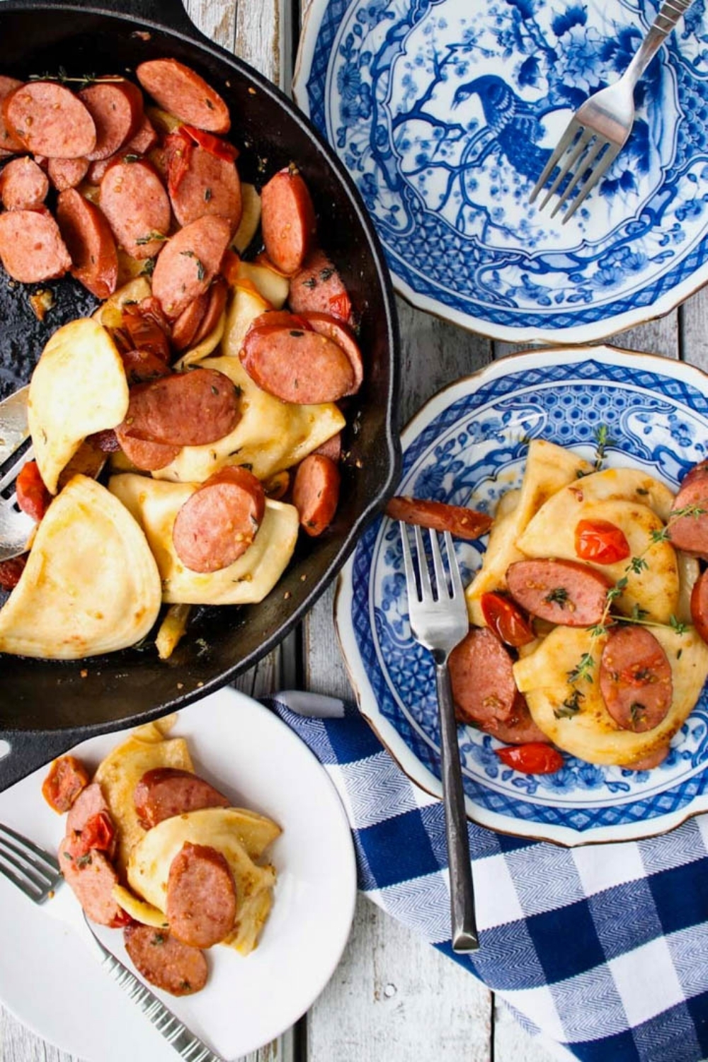 skillet of sausage and pierogis with blue plates on side. One plate is empty