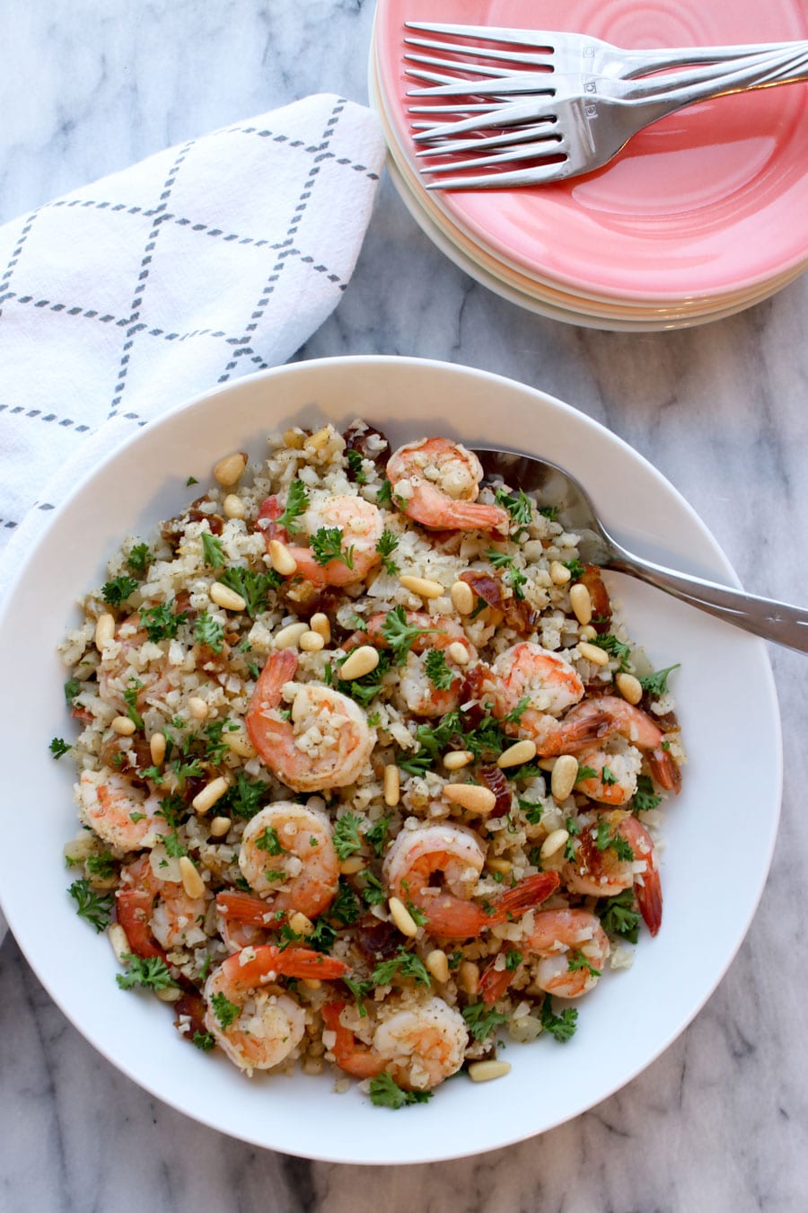 Bowl of cauliflower rice next to a stack of dishes and forks