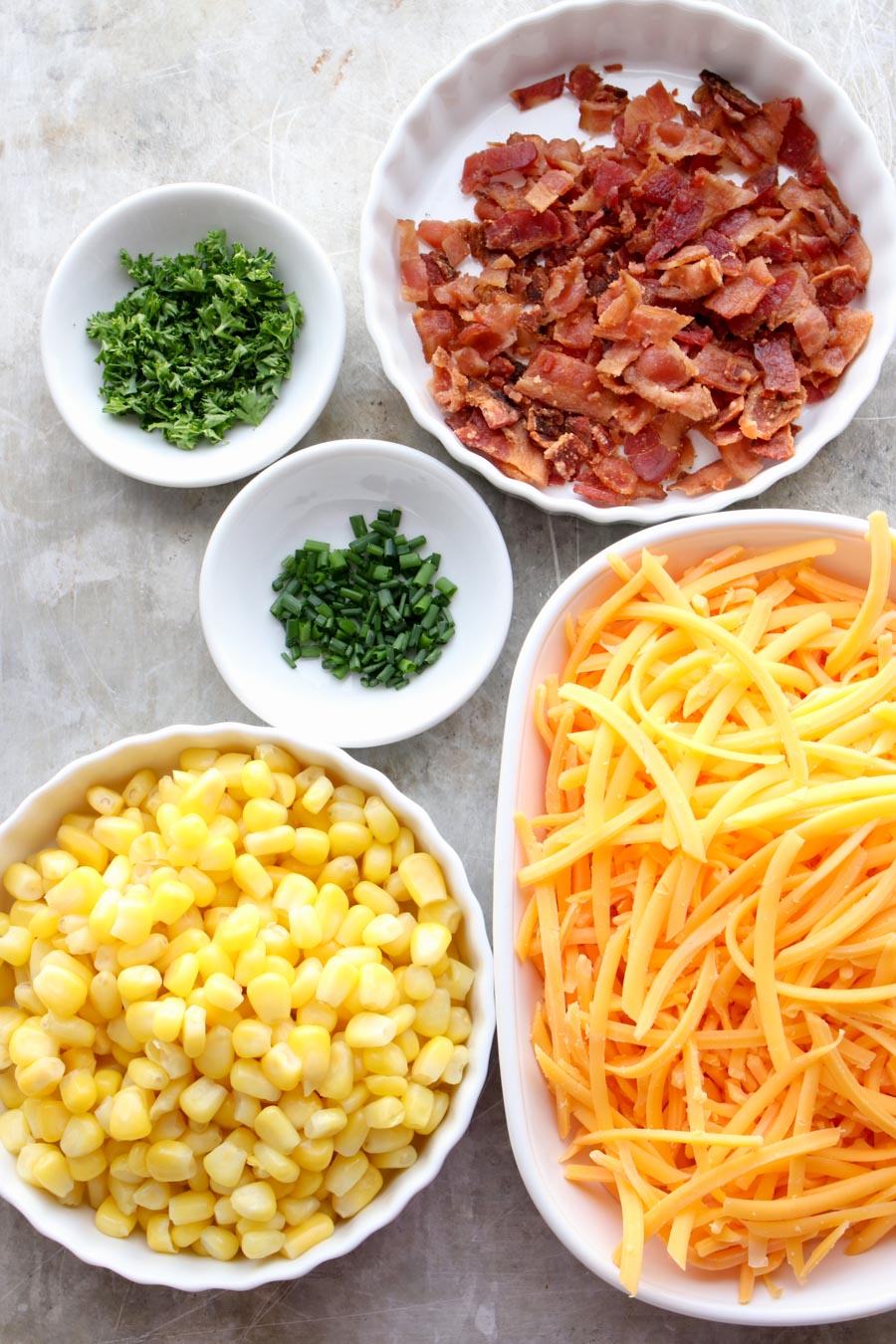 bowls with the ingredients of the pancakes - cheese, corn, chives, parsley and bacon