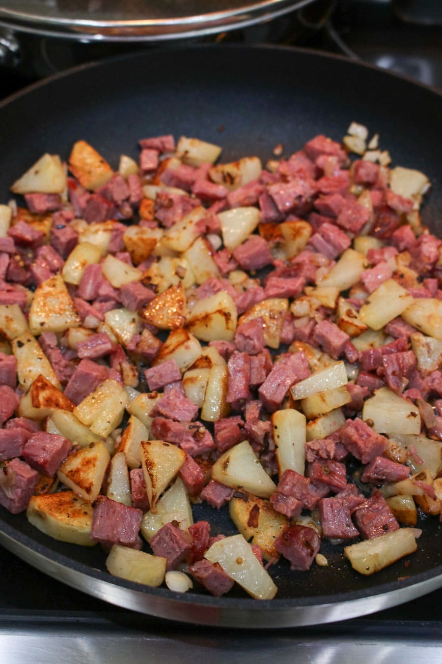 Diced potatoes, onions, and corned beef in a skillet