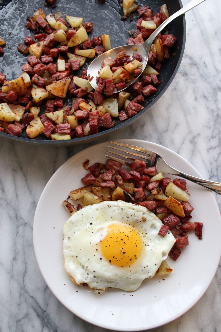 Skilled and a plate of corned beef hash. The plate has an egg on top