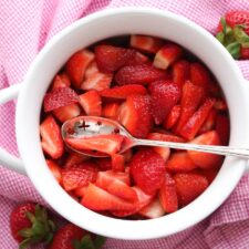 A bowl red strawberries sitting on a pink and white cloth