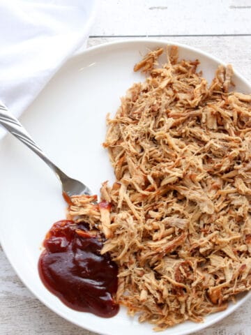 Pulled pork on a white plate with a dollop of BBQ sauce