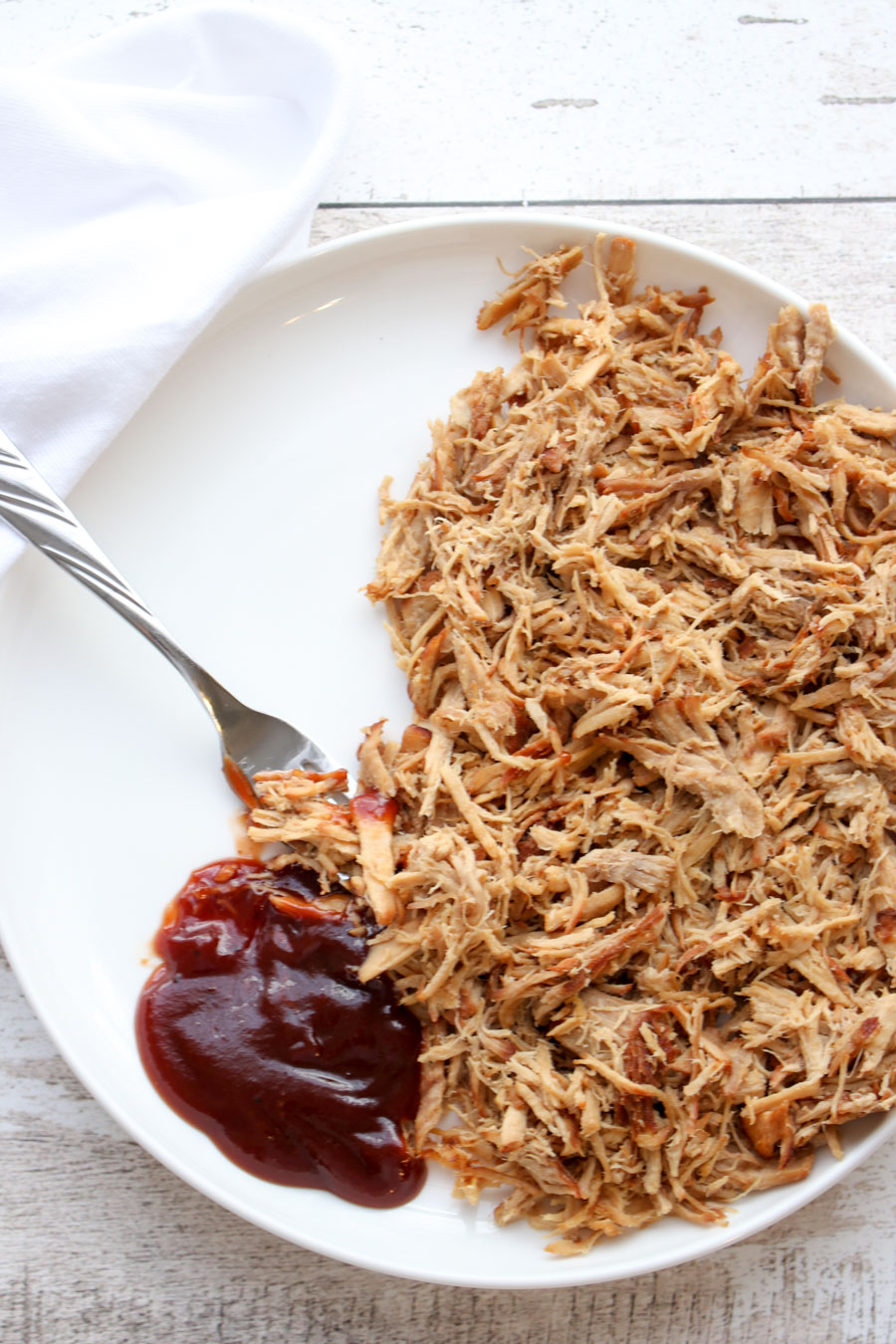 Pulled pork on a white plate with a dollop of BBQ sauce