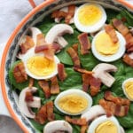 Bowl of spinach salad with eggs, mushrooms, and bacon