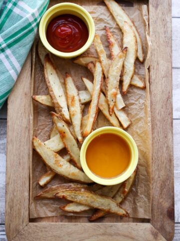 Salt and vinegar fries on a wooden tray with ketchup and vinegar