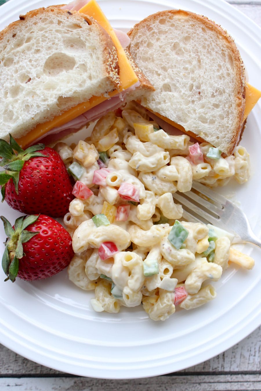 Scoop of macaroni salad on a plate with a sandwich and strawberries