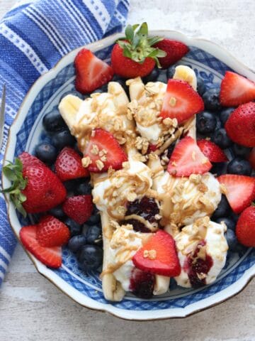 A blue bowl with two bananas filled with yogurt, topped with fruit and granola