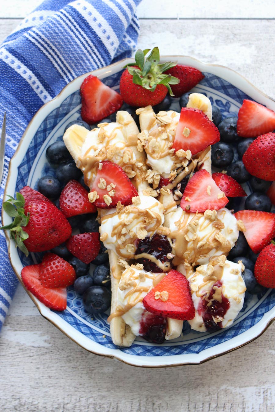 A blue bowl with two bananas filled with yogurt, topped with fruit and granola