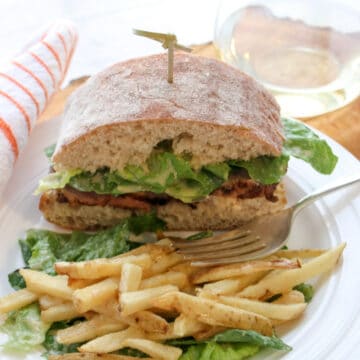 Sandwich and fries on a plate with a glass of white wine in background