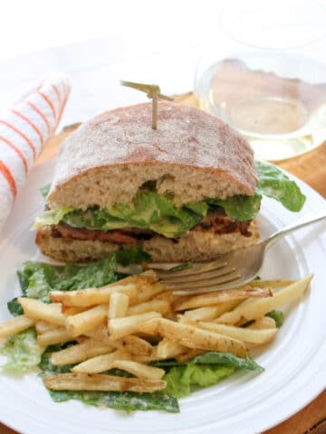 Sandwich and fries on a plate with a glass of white wine in background