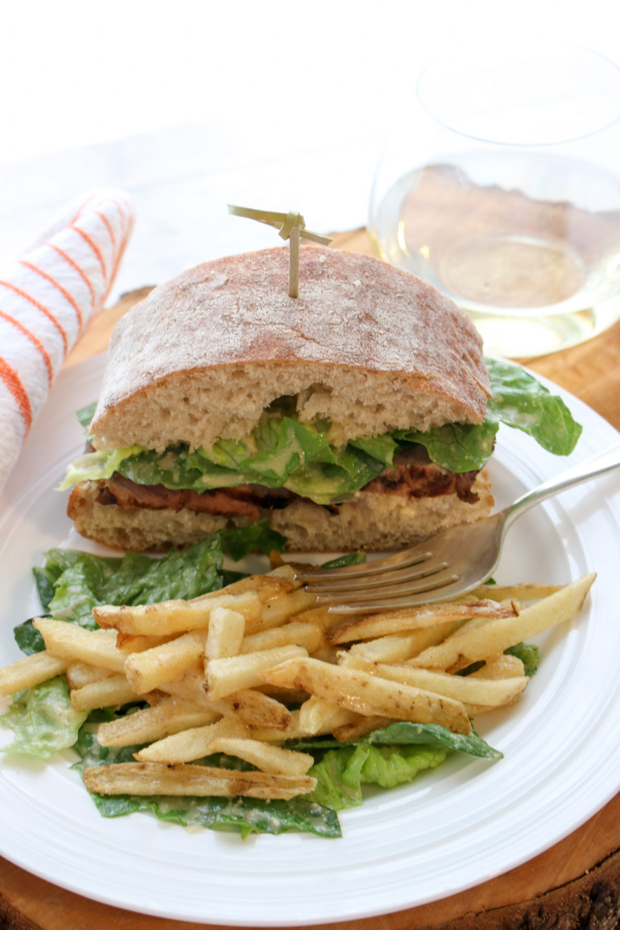 Sandwich and fries on a plate with a glass of white wine in background