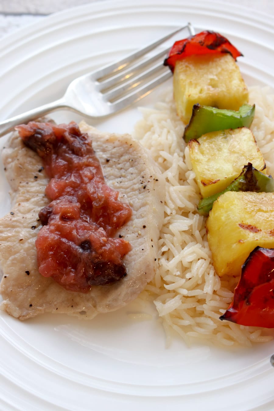 Pork chop topped with chutney. Rice and fruit kabob on the side.