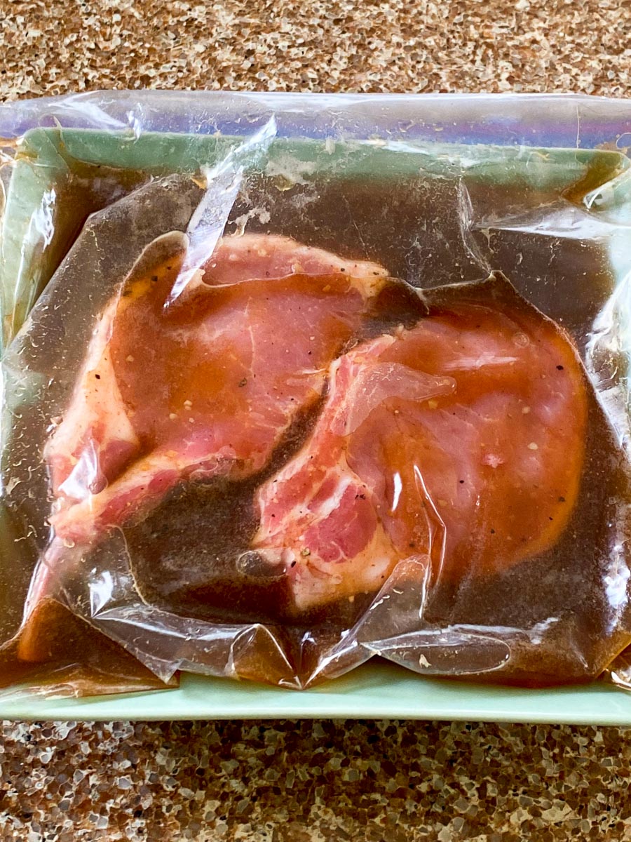 Two pork chops in a zip-top bag filled with marinade