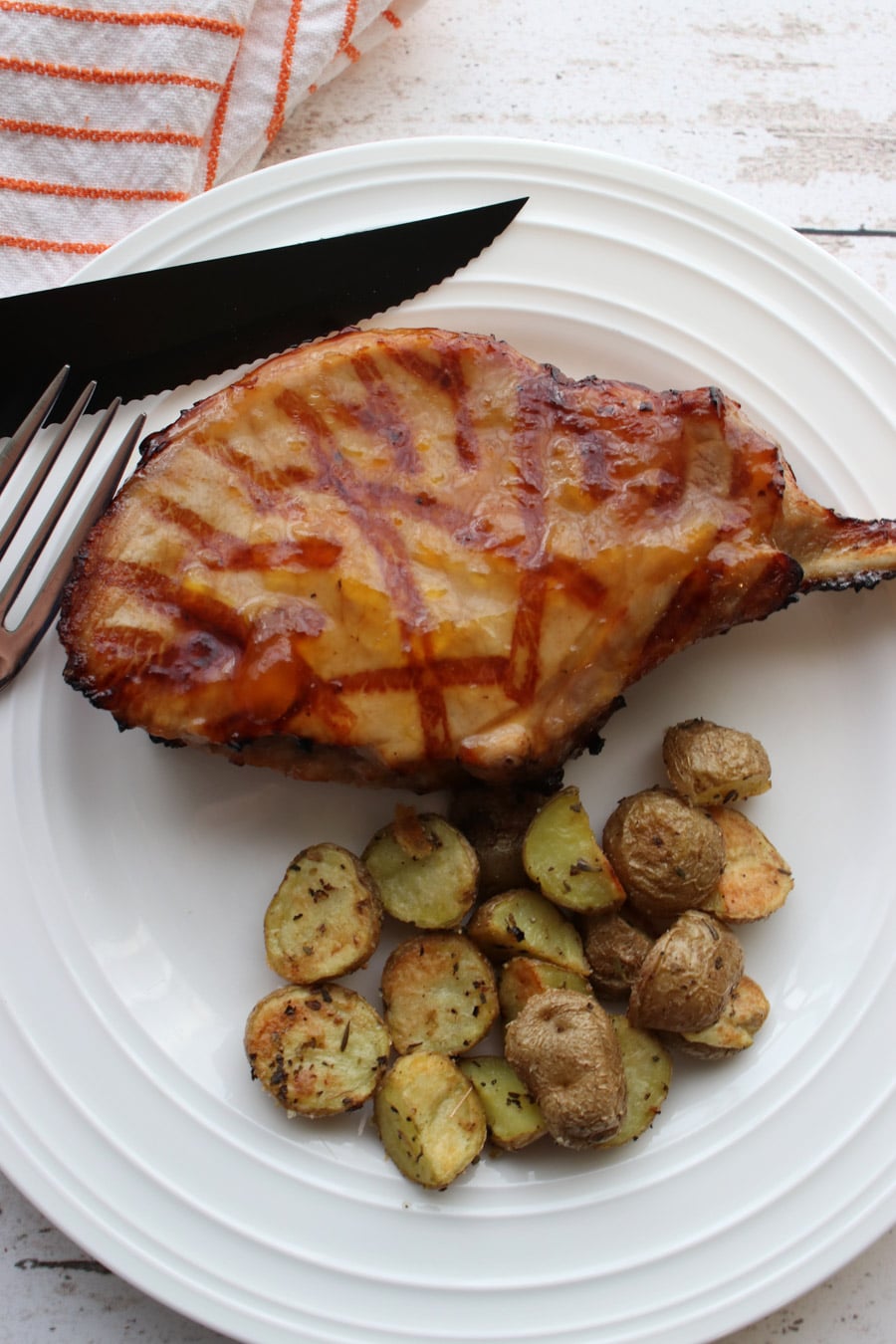 Pork chop and small roasted potatoes on a white plate