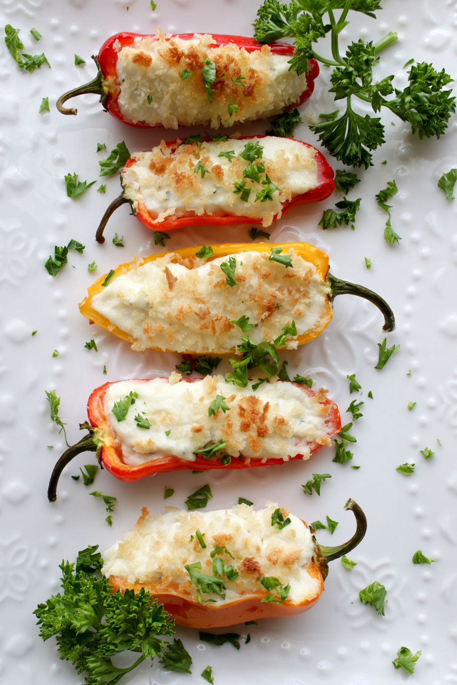 five stuffed red peppers with cheese on a white plate with parsely