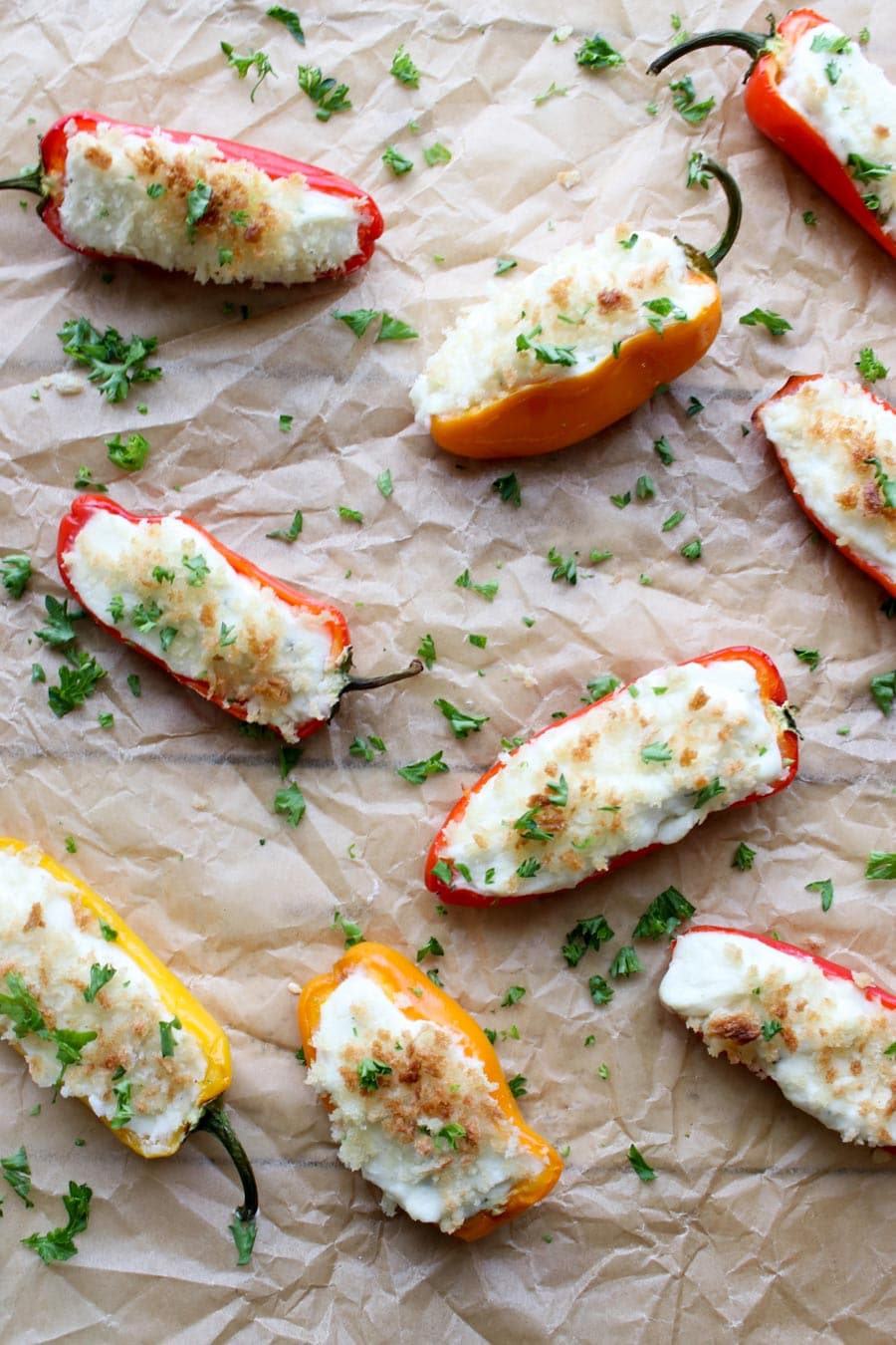 Overhead photo of cheese stuffed peppers on a piece of brown parchment papers sprinkled with parsley.