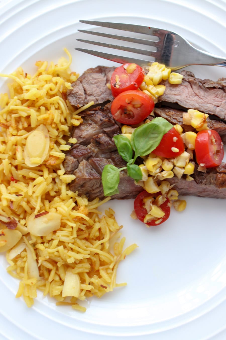 plate of skirt steak topped with salsa with a side of yellow rice