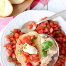 A hand holding a piece of toast topped with tomato bruschetta and cheese