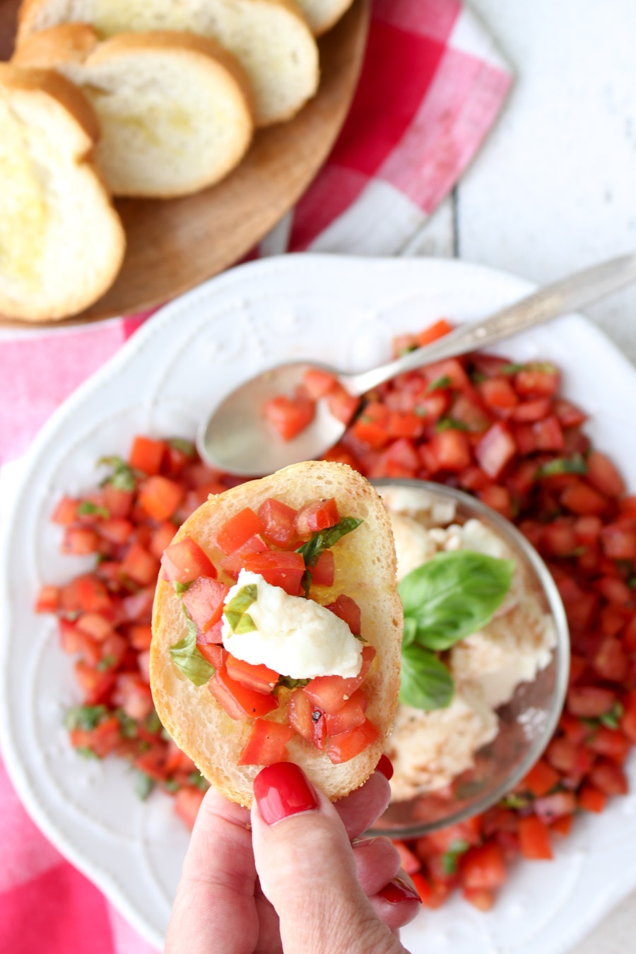 A hand holding a piece of toast topped with tomato bruschetta and cheese