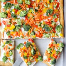 Veggie pizza on a sheet pan with three square pieces cut out