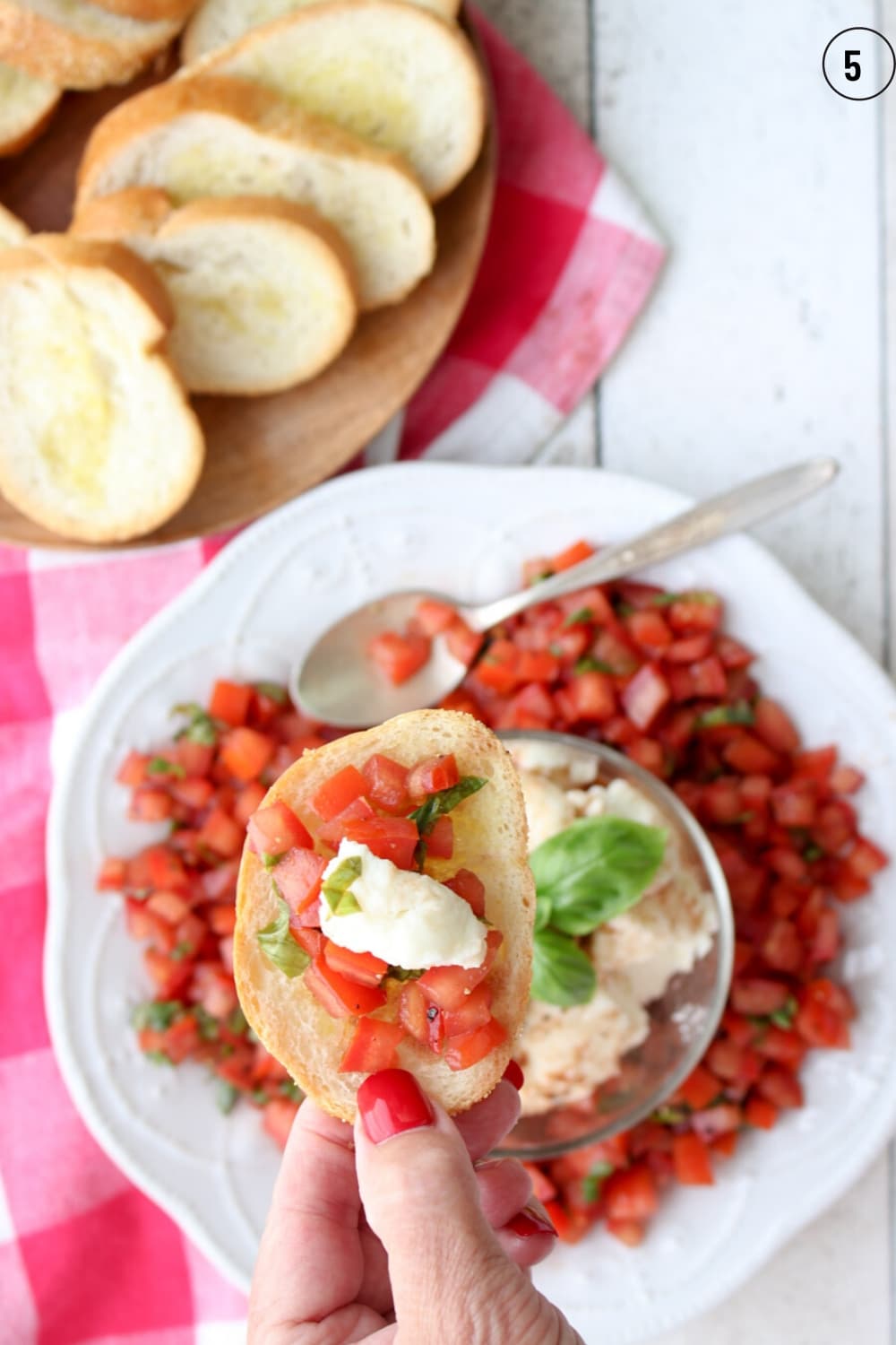 A hand holding a piece of toast topped with tomato bruschetta and cheese