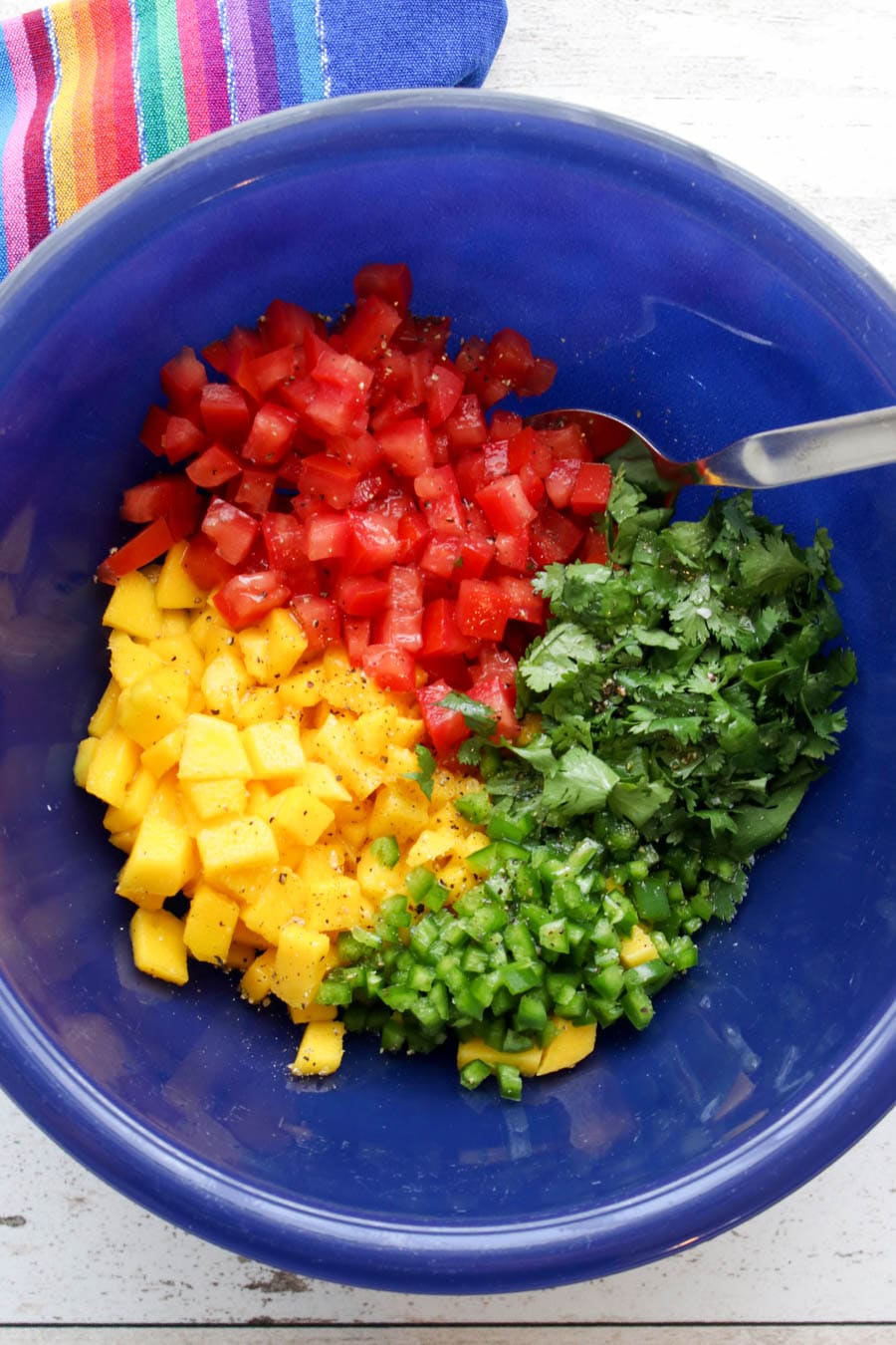 Blue bowl with all of the prepared ingredients to make mango salsa