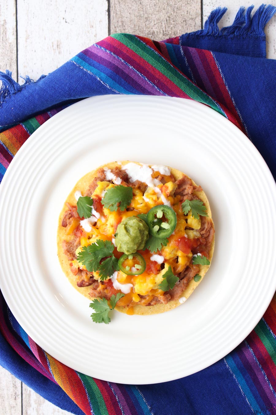 Huevos Rancheros on a white plate the is sitting on a colorful cloth