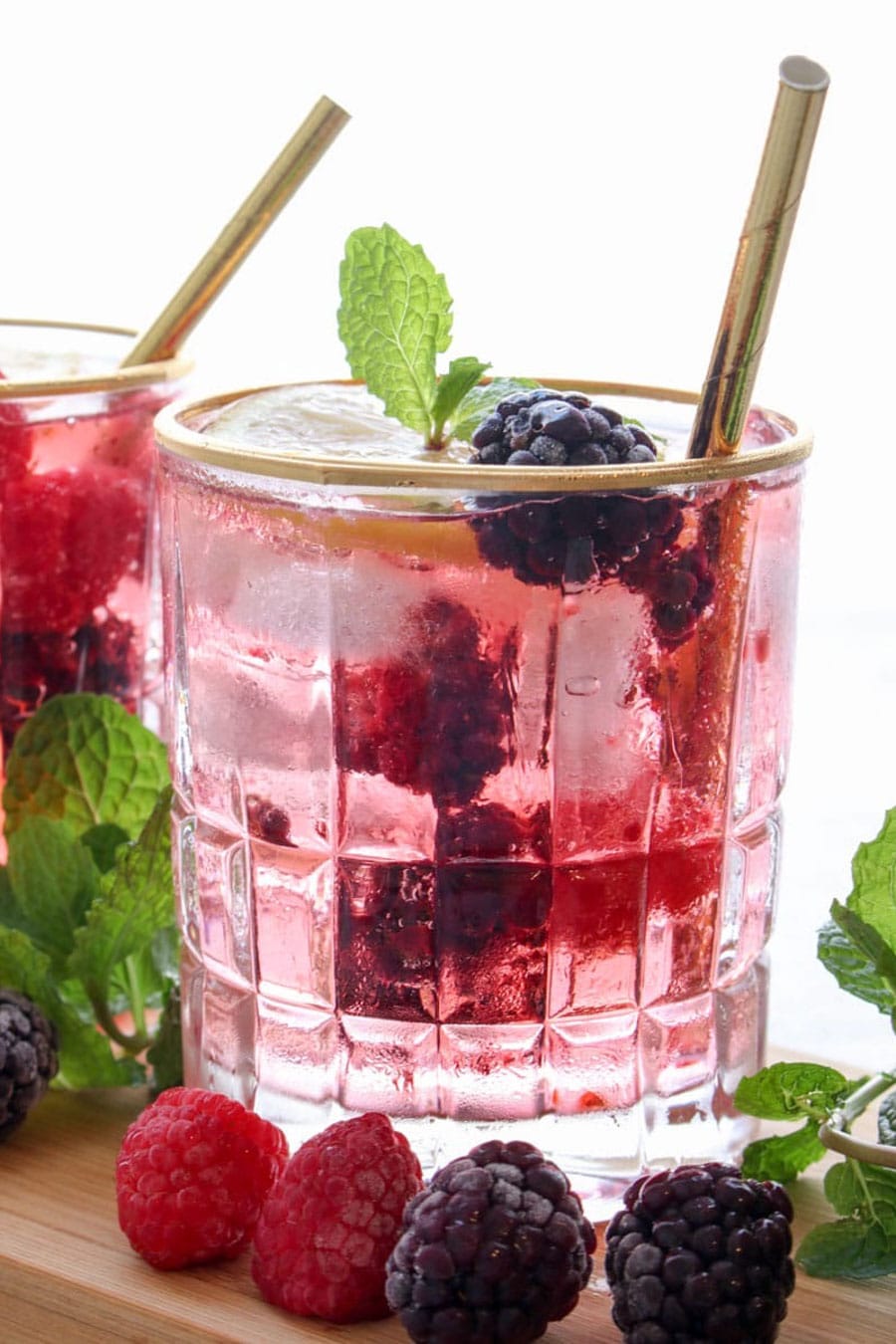 Berry gin cocktail with a gold straw and mint leaves