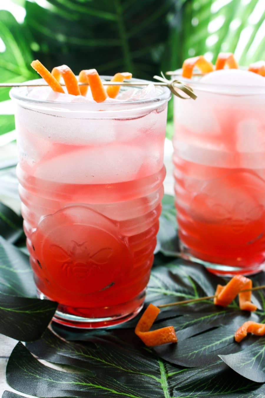 two glasses filled with pink cocktail sitting on big green leaves