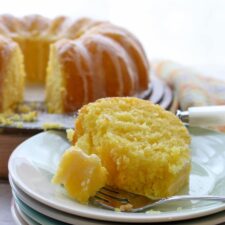 slice of lemon cake on a stack of plates with whole cake in background