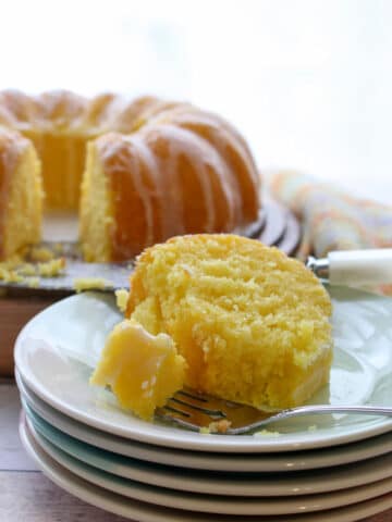 slice of lemon cake on a stack of plates with whole cake in background