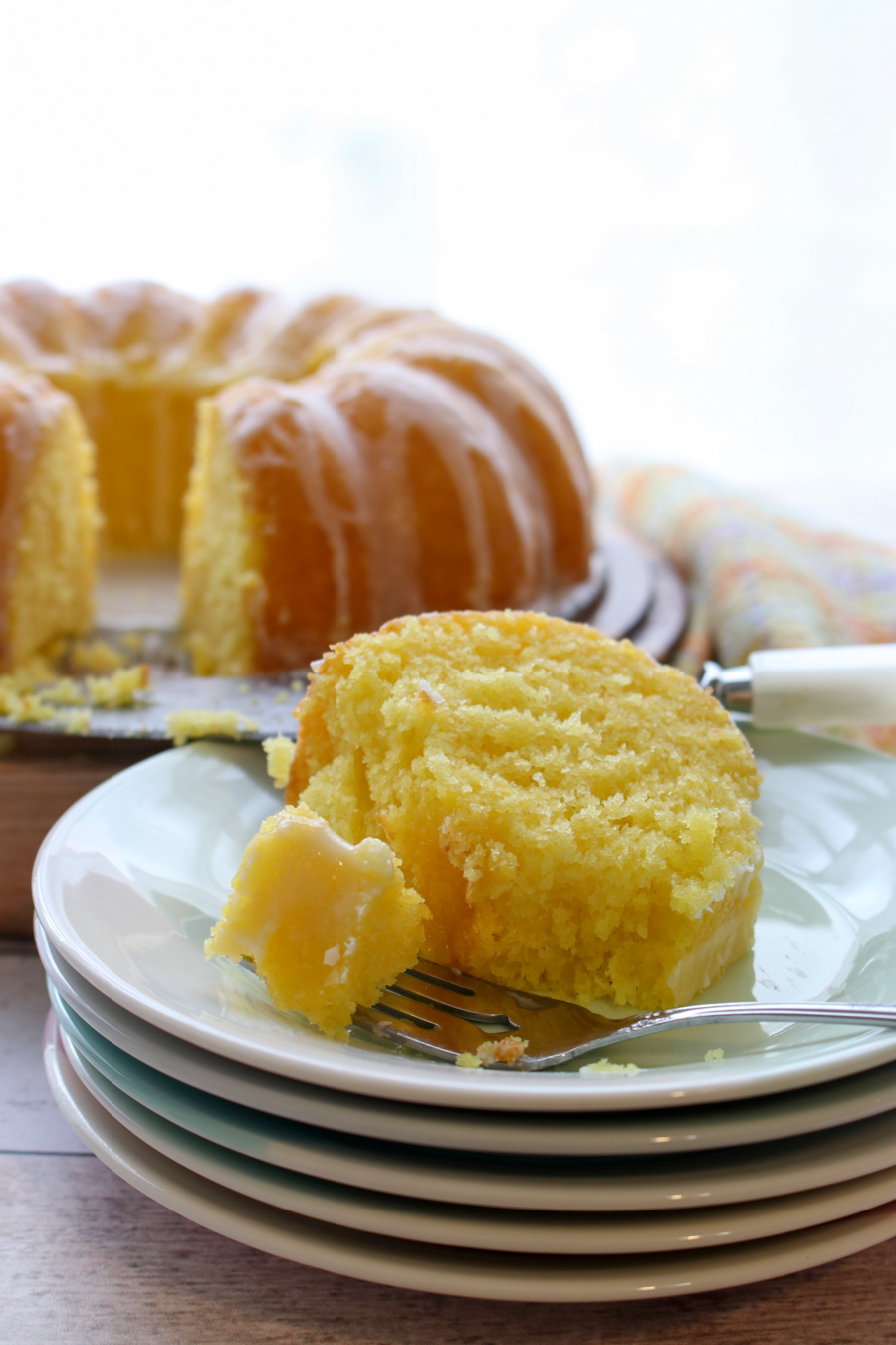 slice of lemon cake on a stack of plates with whole cake in background