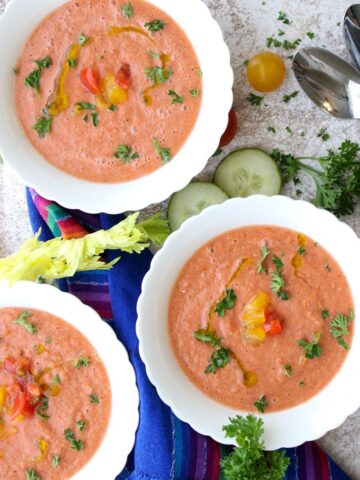 Three bowls of gazpacho topped with tomatoes and parsley