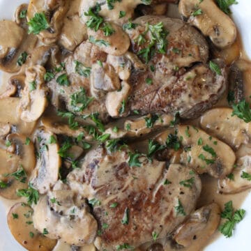 Two steaks on a platter covered with a creamy mushroom sauce