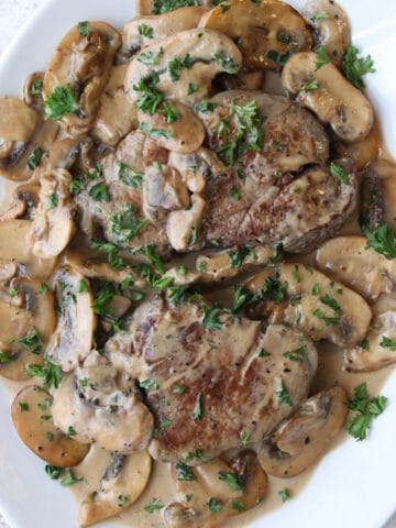 Two steaks on a platter covered with a creamy mushroom sauce