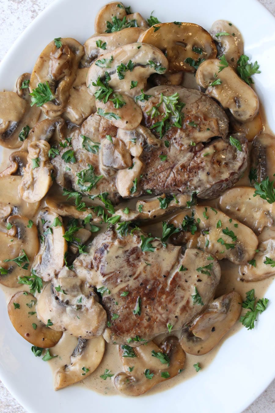 Two steaks on a platter covered with a creamy mushroom sauce