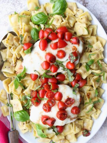 White platter filled with ravioli topped with chicken, cheese tomatoes and basil