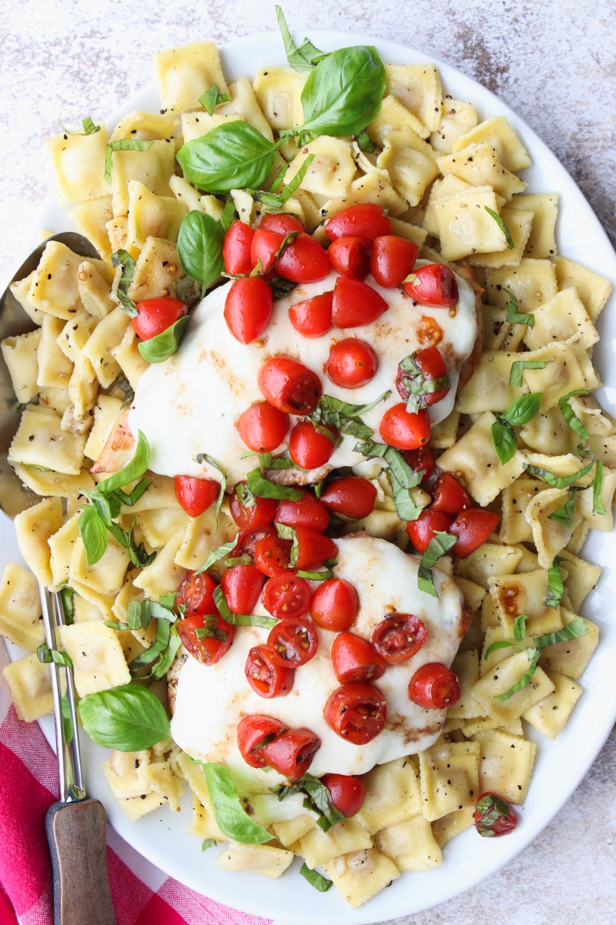 White platter filled with ravioli topped with chicken, cheese tomatoes and basil