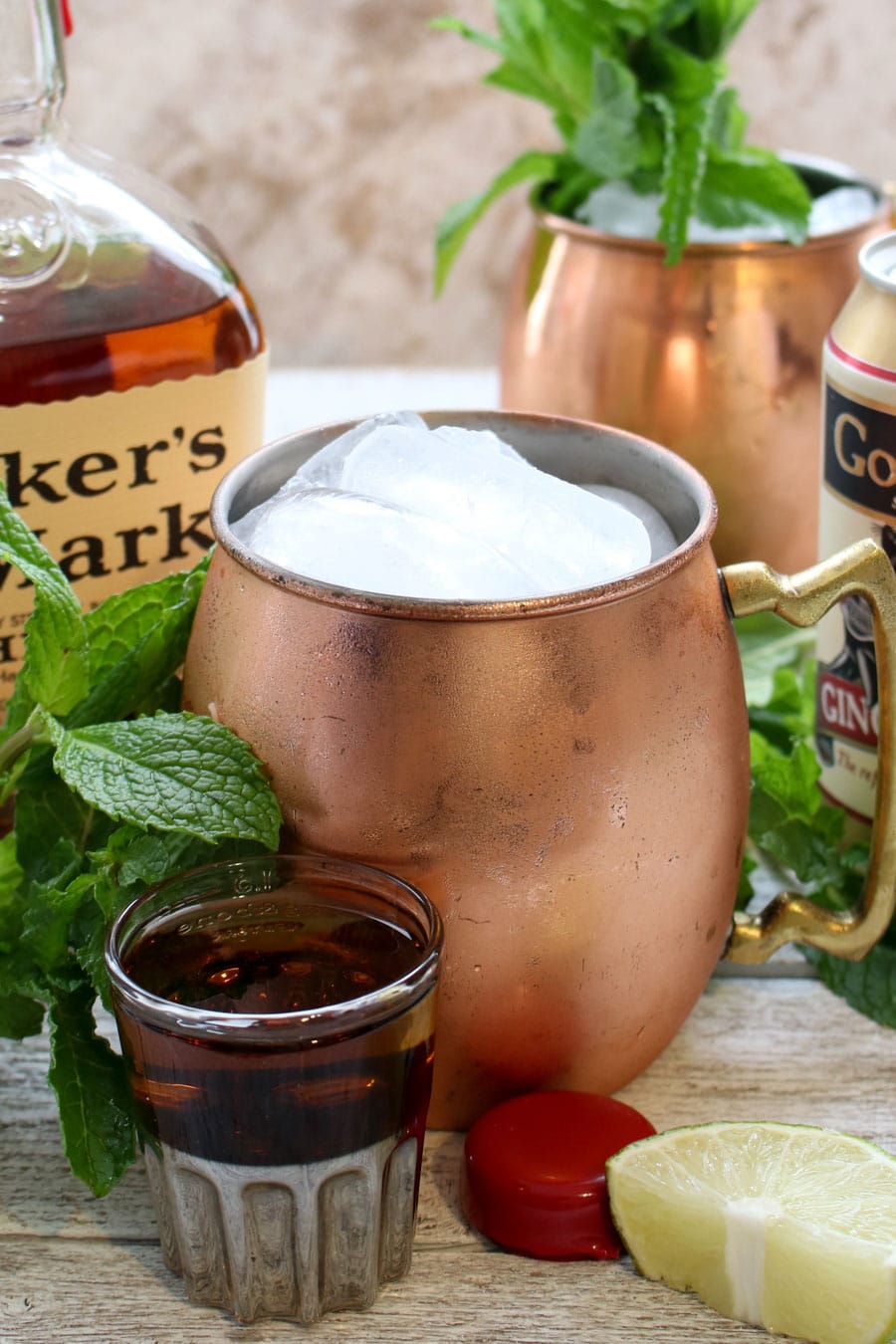 Copper mug filled with ice and a shot of bourbon in front with the bottle of bourbon in background