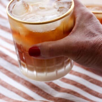 Woman's hand holding a glass of iced Irish coffee over a stripped background