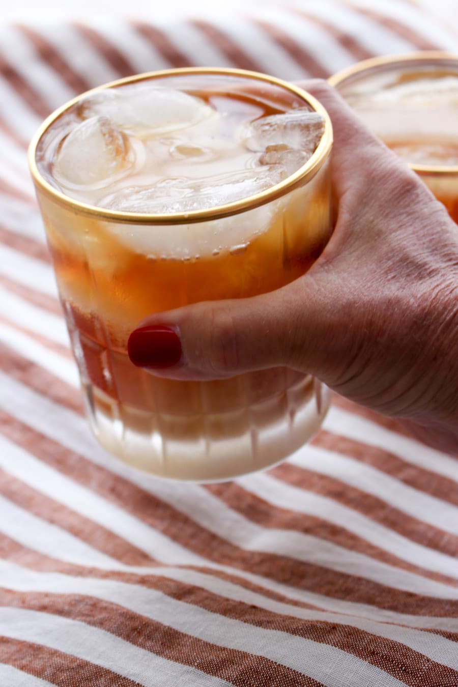 Woman's hand holding a glass of iced Irish coffee over a stripped background