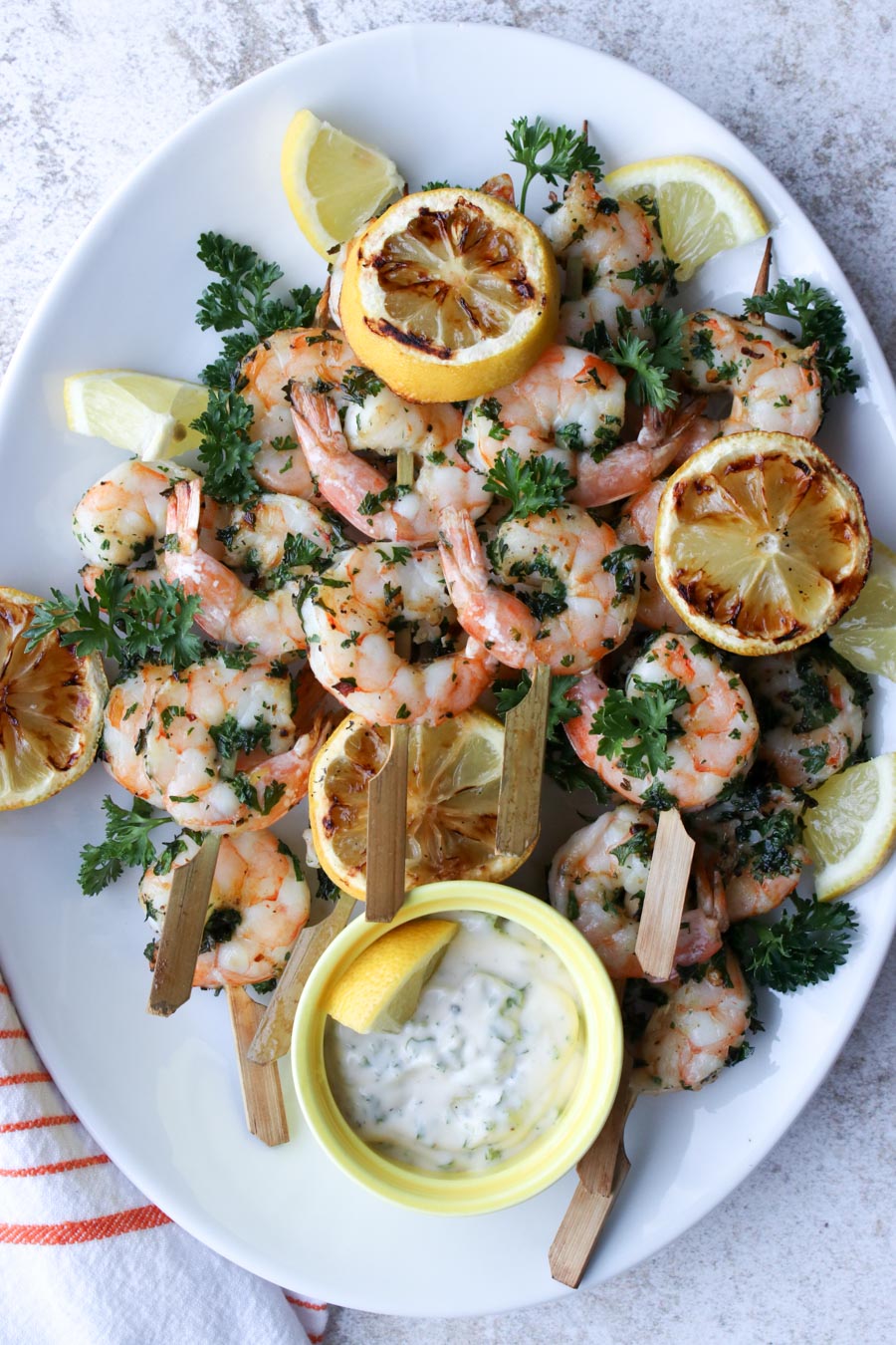 white platter with shrimp skewers and grill lemons on it with a side of white dipping sauce