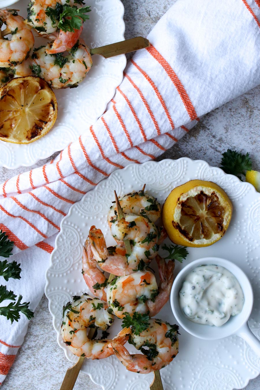 White plate with two shrimp skewers, a grilled lemon half, and some white sauce