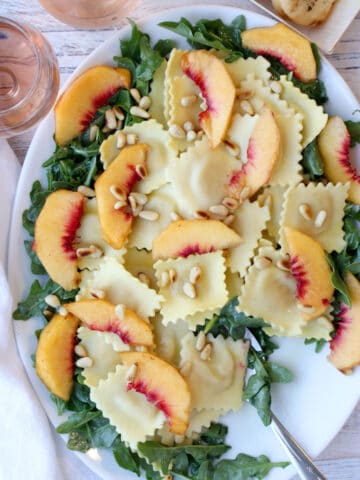 White platter with ravioli, arugula, peaches