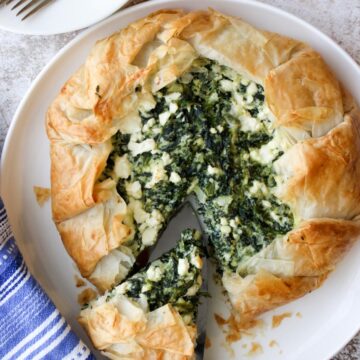 Spinach galette on a white plate with one slice being cut out