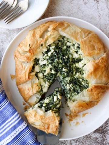 Spinach galette on a white plate with one slice being cut out