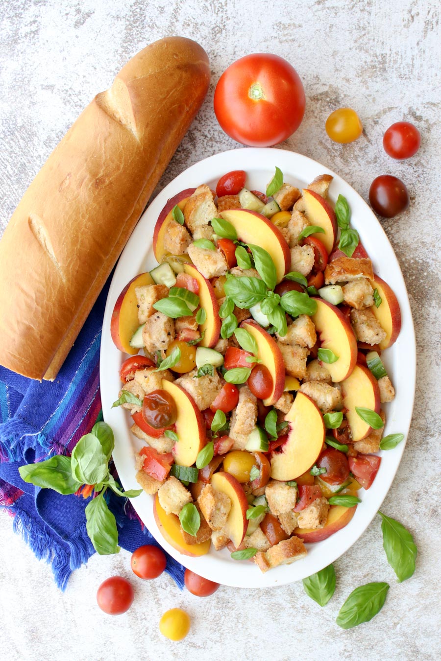 Bread salad on a white platter sitting next to a baguette