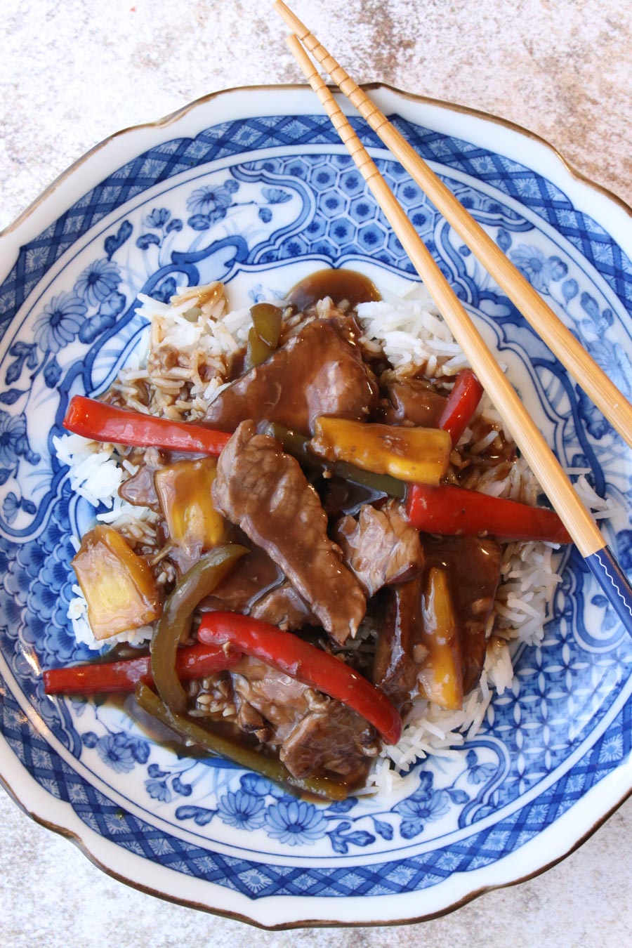 Blue plate with white rice and pepper steak and chop sticks on the side of plate